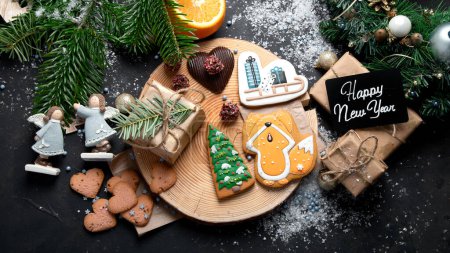 Téléchargez les photos : Biscuits de Noël, chocolat de Noël traditionnel Pains d'épice avec décoration de vacances, cadeaux, branche d'arbre de Noël sur fond sombre, vue sur le dessus. - en image libre de droit