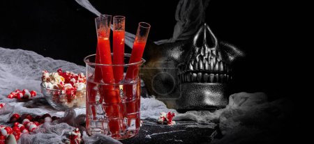 Foto de Cóctel sangriento en tubos de vidrio para la celebración de la fiesta de Halloween con aperitivos sobre un fondo negro. Panorama. - Imagen libre de derechos