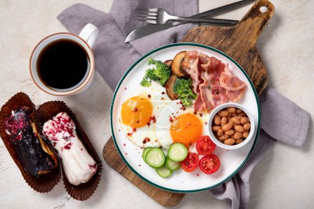 Photo for Traditional Englis breakfast plate with bacon strips, sunny side up eggs, vegetables and cake on light background. - Royalty Free Image