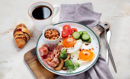 Téléchargez les photos : Assiette de petit déjeuner traditionnelle Englis avec lanières de bacon, œufs ensoleillés, légumes et gâteau sur fond clair. - en image libre de droit