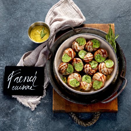 Téléchargez les photos : Escargots au beurre d'herbes, cuisine traditionnelle française au persil et pain sur fond gris. Vue du dessus. - en image libre de droit