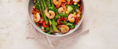 Photo for Stir fry vegetables and shrimps in a white plate on a light background. Top view. Panorama with copy space. - Royalty Free Image