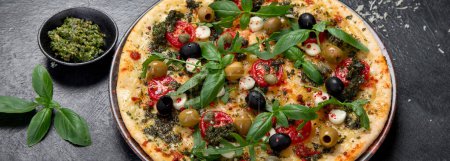 Foto de Pizza Margherita con tomates, queso, albahaca y aceitunas sobre fondo negro. Pizza vegetariana fina casera. Vista superior. Panorama. - Imagen libre de derechos