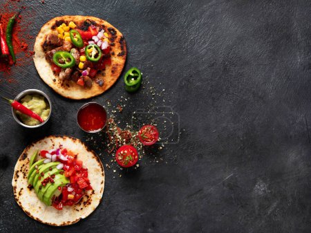 Téléchargez les photos : Tacos avec salsa, légumes et avocat sur fond noir. Vue du dessus, espace de copie. - en image libre de droit
