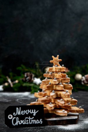 Photo for Homemade Gingerbread cookies. Christmas tree, decorated with icing and sugar decorations on a black background. Top view. - Royalty Free Image