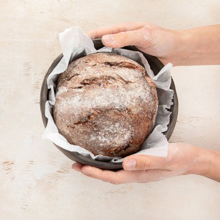 Foto de Panadero o cocinero sosteniendo pan recién horneado en las manos sobre un fondo claro. Concepto de cocina. - Imagen libre de derechos