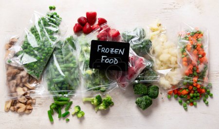 Téléchargez les photos : Ensemble de différents légumes congelés dans des sacs en plastique sur fond blanc. Vue du dessus. - en image libre de droit
