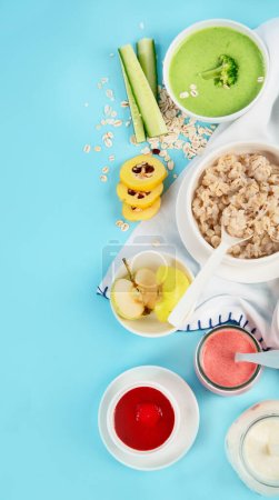 Bowls with healthy baby food on blue background. Top view, copy space.