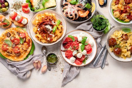Téléchargez les photos : Table complète de repas italiens sur assiettes Pizza, pâtes, raviolis, salade caprese et bruschetta tomate sur fond blanc. Vue du dessus. - en image libre de droit