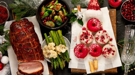 Foto de Jamón al horno con verduras y rosquillas sobre fondo oscuro. Comida navideña. Vista superior. - Imagen libre de derechos