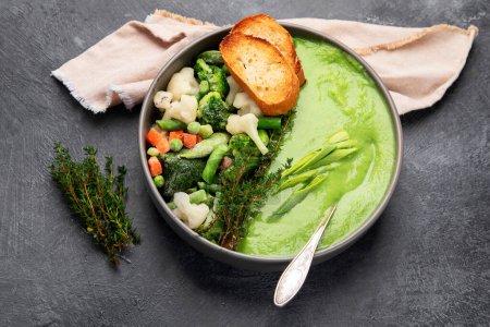 Téléchargez les photos : Soupe verte à la crème de légumes dans un bol gris sur fond gris, vue de dessus. Purée de légumes verts à la soupe végétalienne. Aliments végétariens et diététiques. - en image libre de droit