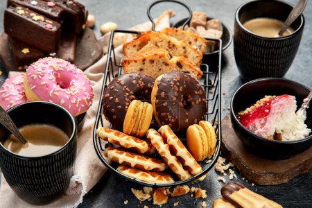 Foto de Café blanco con deliciosa galleta, rosquillas, tarta, azúcar, gofres. Bebida caliente con dulces sobre fondo oscuro. - Imagen libre de derechos