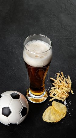 Téléchargez les photos : Bière et snack avec ballon de football sur fond noir. Jeu de football nuit nourriture. - en image libre de droit