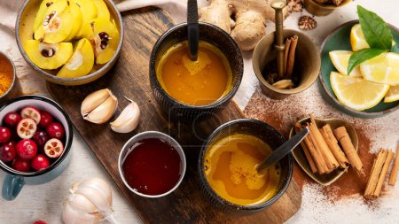 Téléchargez les photos : Tasses de thé épicé au curcuma sain avec des ingrédients : citron, gingembre, bâtonnets de cannelle et miel sur fond blanc, vue de dessus. Remède stimulant immunitaire. - en image libre de droit
