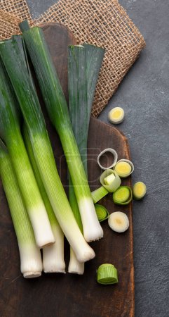 Photo for Whole and cut fresh leeks on a dark background, vegetarian food, healthy eating. Top view. Copy space. - Royalty Free Image