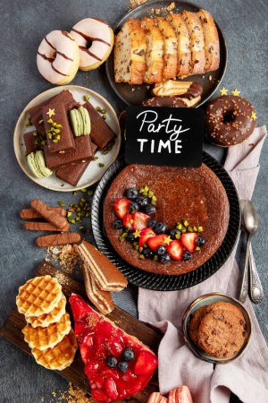 Téléchargez les photos : Gâteau savoureux, biscuits, gaufres, macarons, muffins. Délicieux desserts sur fond sombre. Concept de nourriture. Vue du dessus - en image libre de droit