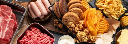 Photo for Saturated and trans. Unhealthy food. Sausage, potato, meat, cheese, popcorn, cookies, cream on dark background. Banner, top view. - Royalty Free Image
