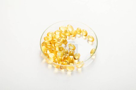 Foto de Placa de Petri con cápsulas de aceite de pescado en ella. Concepto de vitamina d, vitaminas omega sobre un fondo blanco. Vista superior. - Imagen libre de derechos