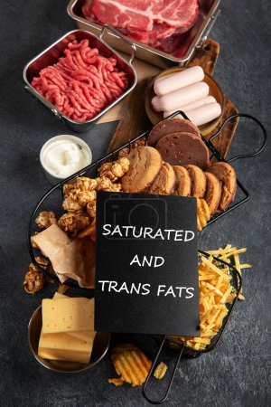 Photo for Saturated and trans. Unhealthy food. Sausage, potato, meat, cheese, popcorn, cookies, cream on dark background. - Royalty Free Image