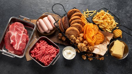 Photo for Saturated and trans. Unhealthy food. Sausage, potato, meat, cheese, popcorn, cookies, cream on dark background. Top view. - Royalty Free Image
