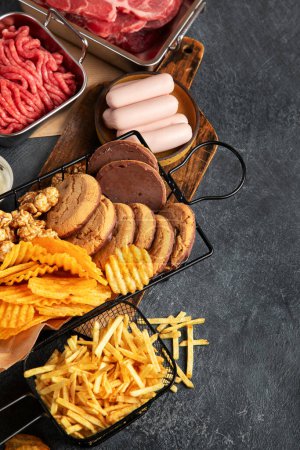 Photo for Saturated and trans. Unhealthy food. Sausage, potato, meat, cheese, popcorn, cookies, cream on dark background. Copy space. - Royalty Free Image