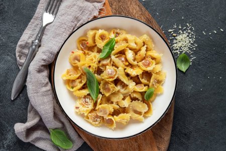Téléchargez les photos : Nourriture italienne traditionnelle. Plat avec raviolis, tomate, tomates séchées au soleil, basiques et fromage râpé. Des pâtes savoureuses. Vue du dessus, espace de copie - en image libre de droit