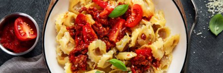Téléchargez les photos : Nourriture italienne traditionnelle. Plat avec raviolis, tomate, tomates séchées au soleil, basiques et fromage râpé. Des pâtes savoureuses. Vue du dessus - en image libre de droit