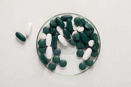 Foto de Varias píldoras de colores en placa de Petri aislado en blanco, vista superior. Apoyo a la salud. Laboratorio de farmacia y concepto de investigación farmacéutica. - Imagen libre de derechos