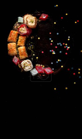 Photo for Ramadan food on a large plate. Arabic sweets - lokum, fruit marmalade, baklava on a black background. Top view - Royalty Free Image