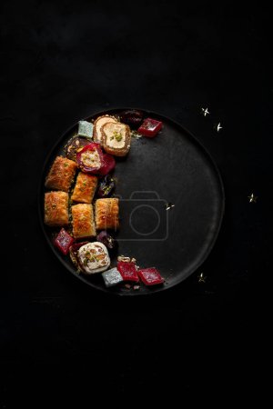 Foto de Comida Ramadán en un plato grande. Los dulces árabes - lokum, la mermelada de frutas, el baklava sobre el fondo negro. Vista superior, espacio de copia - Imagen libre de derechos