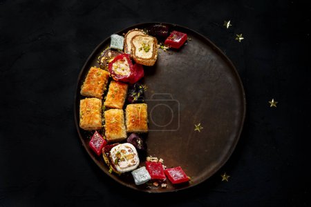 Téléchargez les photos : Ramadan nourriture sur une grande assiette. Bonbons arabes - lokum, confiture de fruits, baklava sur fond noir. Vue du dessus - en image libre de droit
