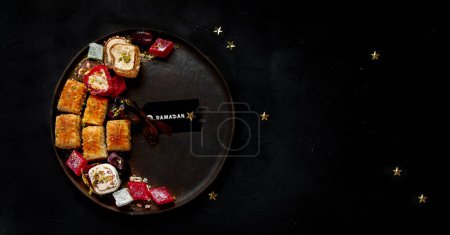 Photo for Ramadan food on a large plate. Arabic sweets - lokum, fruit marmalade, baklava on a black background. Top view, copy space - Royalty Free Image