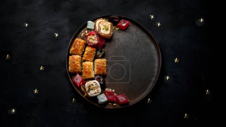 Foto de Comida Ramadán en un plato grande. Los dulces árabes - lokum, la mermelada de frutas, el baklava sobre el fondo negro. Vista superior, espacio de copia - Imagen libre de derechos
