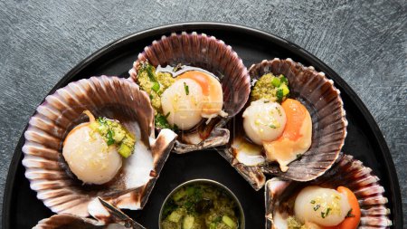 Photo for Baked scallops in seashells with sauce and spices on a black stone plate on a dark background. Seafood. Top view. - Royalty Free Image