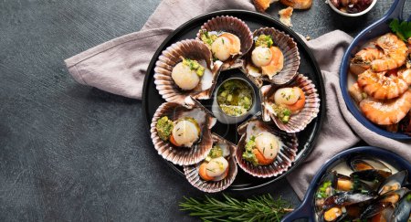 Photo for Baked scallops in seashells with sauce and spices on a black stone plate on a dark background. Seafood. Top view. Copy space. - Royalty Free Image
