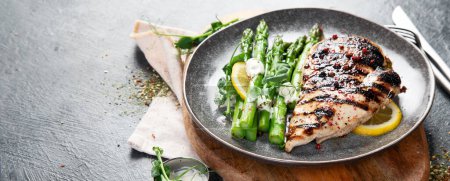 Photo for Grilled chicken breast and garnish of asparagus on a dark background. Top view. Panorama with copy space. - Royalty Free Image
