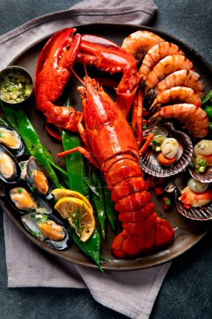 Photo for Big red lobster on plate with shrimp and mussels with lemon, souce pesto and bread. Seafood concept. Top view. - Royalty Free Image