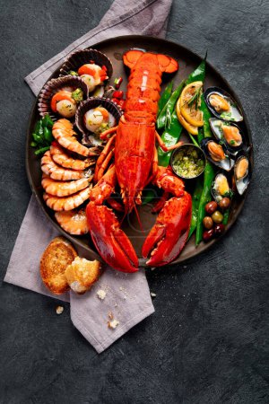 Téléchargez les photos : Grand homard rouge sur assiette avec crevettes et moules au citron, pesto à la soupe et pain. Concept de fruits de mer. Vue du dessus. - en image libre de droit