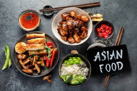 Foto de Pollo teriyaki sobre fondo oscuro con salsas, arroz, verduras y semillas de sésamo. Comida asiática. Vista superior. - Imagen libre de derechos
