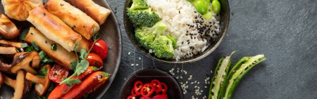 Foto de Pollo teriyaki sobre fondo oscuro con salsas, arroz, verduras y semillas de sésamo. Comida asiática. Vista superior. Panorama con espacio de copia. - Imagen libre de derechos