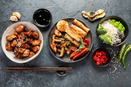 Foto de Pollo teriyaki sobre fondo oscuro con salsas, arroz, verduras y semillas de sésamo. Comida asiática. Vista superior. - Imagen libre de derechos