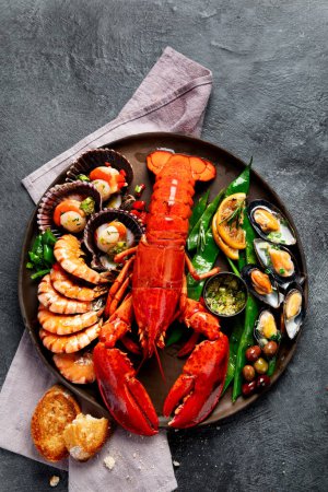 Téléchargez les photos : Grand homard rouge sur assiette avec crevettes et moules au citron, pesto à la soupe et pain. Concept de fruits de mer. Vue du dessus, espace de copie - en image libre de droit