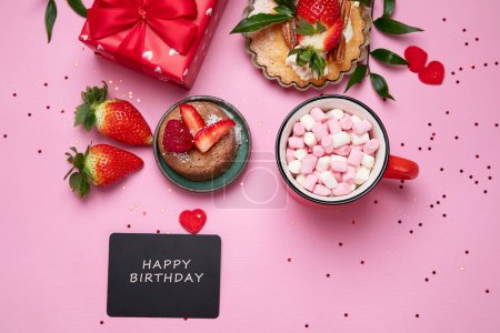Foto de Fondo rosa festivo con cupcake, fresas, chocolates, bebida caliente. Celebración de cumpleaños. Vista superior - Imagen libre de derechos