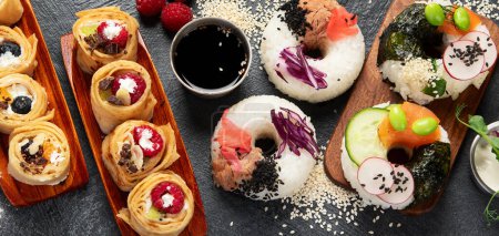 Téléchargez les photos : Nourriture hybride tendance sur fond sombre. Crêpe roulée aux sushis, sushis aux beignets, pizza aux pâtes. Vue du dessus - en image libre de droit