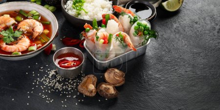 Téléchargez les photos : Table traditionnelle asiatique. Rouleau de printemps, riz, crevettes, sushis, légumes, viande sur fond sombre. espace de copie - en image libre de droit