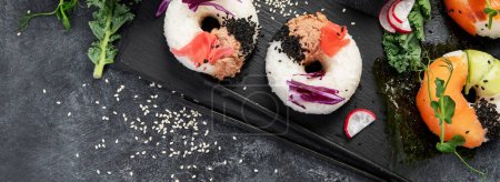 Foto de Rosquillas de sushi sobre un fondo oscuro. Comida de tendencia híbrida. Vista superior, espacio de copia - Imagen libre de derechos