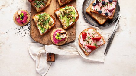 Photo for Various of vegan sandwiches on a light background. Healthy toasts with cheese, avocado, arugula, tomatoes and hummus. Healthy eating. Top view. Copy space. - Royalty Free Image