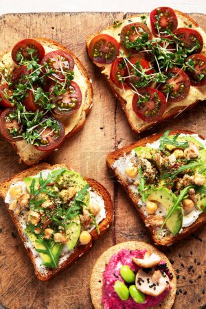 Photo for Various of vegan sandwiches on a light background. Healthy toasts with cheese, avocado, arugula, tomatoes and hummus. Healthy eating. Top view. - Royalty Free Image