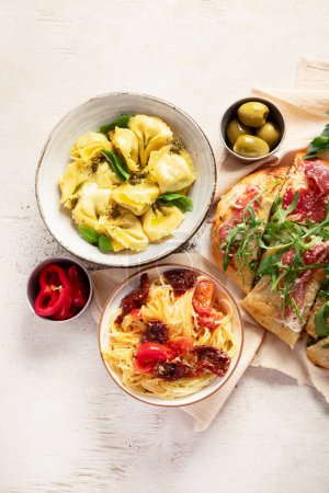 Foto de Mesa completa de comidas italianas en platos pizza, pasta, ravioles, ensalada y focaccia sobre fondo blanco. Vista superior - Imagen libre de derechos