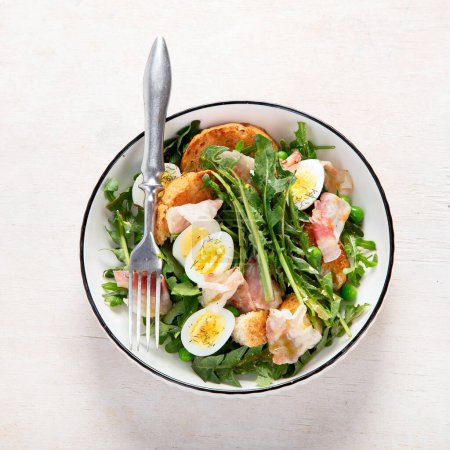Téléchargez les photos : Salade fraîche estivale à base de feuilles de pissenlit, œufs, bacon et pain sur fond clair. Vue du dessus - en image libre de droit